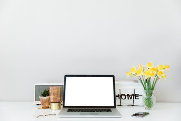 Top view of white office desk with laptop, smartphone, cup of coffee and supplies. Top view with copy space. Workspace with phone, laptop, flowers bouquet and glasses. Computer mockup white background