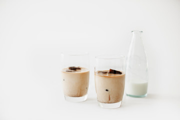 Frozen coffee ice cubes in a glass poured with milk to make a refreshing summer iced coffee drink. White background, isolated, copy space.