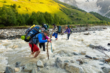 A group of tourists with backpacks crosses a swampy mountain river. Crossing the mountain river...
