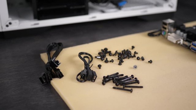 Closeup male hand puts a black cable to a bunch of metal screws, preparing to build a computer in a new white case.