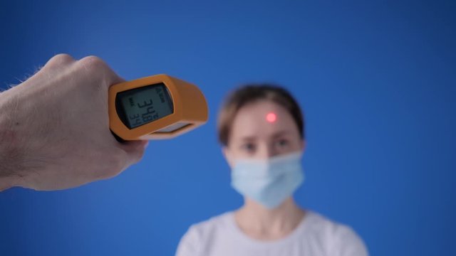 Slow motion: man hand holding yellow pyrometer to measure temperature of woman in medical face mask - close up view, selective focus. Healthcare, measurement, disease, infection, coronavirus concept