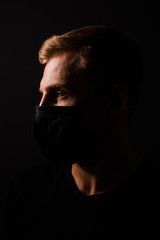 Handsome man in black t-shirt wear black medical mask, gray background. Coronavirus covid-19...