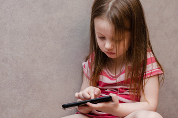 little girl enthusiastically controls the phone. online learning games mobile, ecaucasian,...