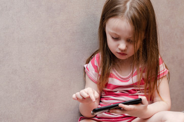 little girl enthusiastically controls the phone. online learning games mobile, ecaucasian,...