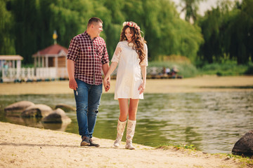 Young happy romantic pregnant couple are walking on nature near lake in summer park. Pregnant woman expecting a baby. Future mom and dad, family. mother's, father's day