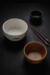 Set of three handmade ceramic bowls with a chopstick. Matte black wood background. 