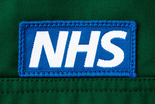 Kent, UK. 11th April 2020. Close up view of NHS logo (National Health Service) badge sewn onto the uniform of a British paramedic uniform shirt.