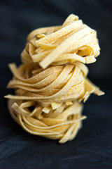 Vertical macro picture of column from traditional Italian raw uncooked pasta Tagliatelle, selective focus. Vegetarian food. Nutrition concept. Italian kitchen. Food preparation. Food pasta background.