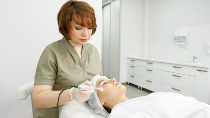 lady in green coat makes microdermabrasion procedure on face of beauty salon patient lying on white couch