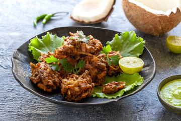 Indian cuisine Indian food. pakora traditional Indian deep-fried snack. pakoras on black plate with coconut chutney sauce curry leaves. national appetiser authentic vegetarian Asian food. travel food