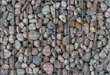 Pattern of many pebble stones behind a metal mesh as a fence design.