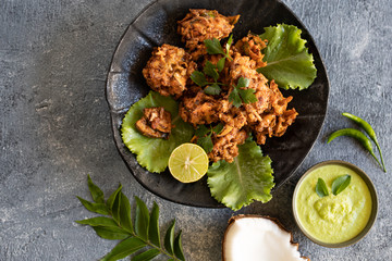Indian cuisine. pakora traditional Indian deep-fried snack. pakoras on black plate with coconut chutney sauce curry leaves. national appetiser authentic vegetarian food. Asian travel food. top view.