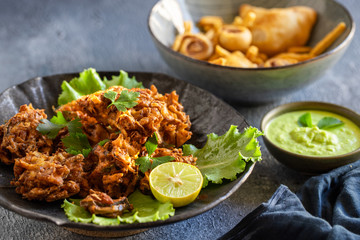 Indian cuisine Indian food. pakora traditional Indian deep-fried snack. pakoras on black plate with coconut chutney sauce curry leaves. national appetiser authentic vegetarian Asian food. travel food