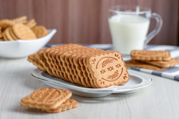 Shortbread cookies rectangular in a white rectangular plate against the background of a mug of milk