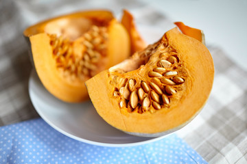 Pumpkin slices on a white plate on a table with blue napkin. Fresh pieces of pumpkin with seeds