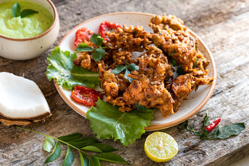 Indian cuisine. pakora traditional Indian deep-fried snack. pakoras on black plate with coconut chutney sauce curry leaves. national appetiser authentic vegetarian food. Asian travel food.