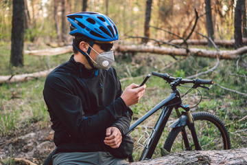 Fototapeta na wymiar Male cyclist wearing respirator face mask with heavy duty protective filter, sitting in forest and uses phone. safety device for protect health. Cyclist in pollution mask from bushfire smoke haze