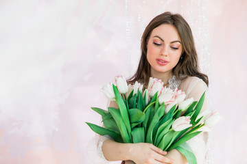 Attractive young woman holding a bouquet of white tulips in her hands on a light pink background with place for text, copy space.