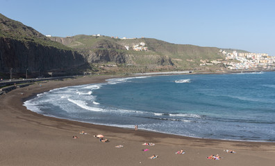 Playa de arena negra con cielo azul y montañas