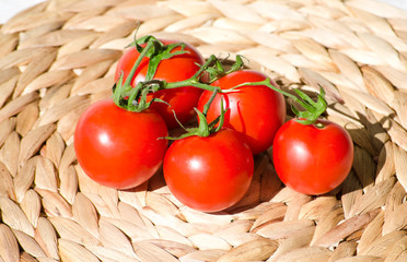 Bright juicy tomatoes closeup. branch with 5 tomatoes on background of woven straw american service. Healthy eating concept, vegetable background. Selective focus image.