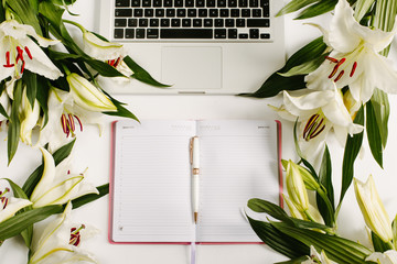 Modern female workspace with laptop, notebook and pen surrounded by flowers. Flat lay composition, overhead view