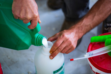 Man pouring liquid from plastic canister into plastic bottle, closeup