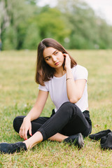 Stylish hipster girl in a white T-shirt sitting on a grass lawn outdoors posing