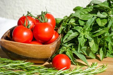 Raw vegetables close up. Top view of fresh tomatoes in a wooden bowl, basil and rosemary. Healthy eating concept, vegetable background. Selective focus image, flat lay.