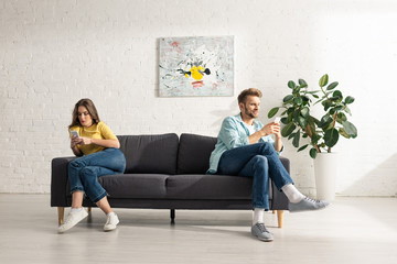 Obraz premium Young couple using smartphones on couch at home