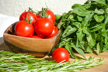 Raw vegetables close up. Top view of fresh tomatoes in a wooden bowl, basil and rosemary. Healthy eating concept, vegetable background. Selective focus image, flat lay.