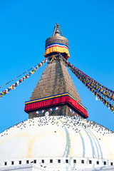 Colorful prayer flags connected Boudha Stupa in Kathmandu, Nepal. The Great stupa Bodnath in Kathmandu, Nepal. Pigeons under the eyes on the top.