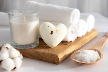 Home beauty essentials & spa concept.  Self-care in quarantine and self-isolation.  White towels folded into a roller on a wooden tray, white candle and scrub salt. bath ball in the shape of a heart. 
