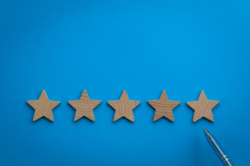 Five Star rating concept with wooden stars on blue paper background
