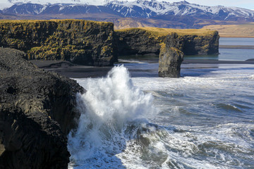 Ocean wave with foam breaks on the coastal rocks in Iceland