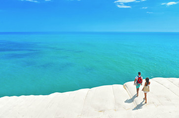 white cliffs naturally made of smooth pug at Scala dei Turchi beach with group of young people with turquoise mediterranean sea and blue cloudy summer sky near Agrigento, Sicily, Italy