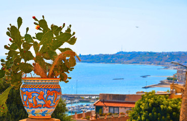 Ceramic pot with cactus on wall and view on the port and sea in front of Sciacca, Sicily, Italy - obrazy, fototapety, plakaty