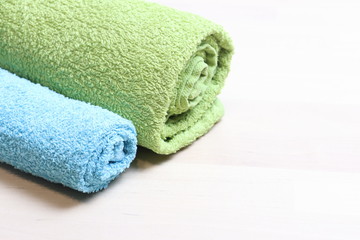 Obraz na płótnie Canvas two terry towels in green and blue, twisted into a roll, lie on a light surface. Cleanliness, bath accessories, freshness, relaxation at home. Lighted, place for text.