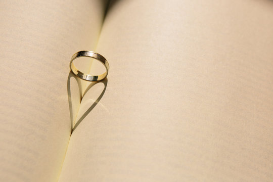 Gold wedding ring forming a heart with the shadow on an old book with yellowed pages. Old picture. Copy space