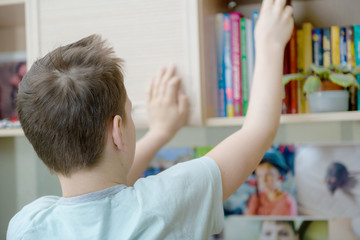 Teen boy in his room taking a book from a shelf
