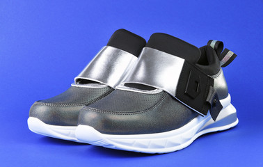 Women's stylish silver sneakers with a white sole on a blue background.