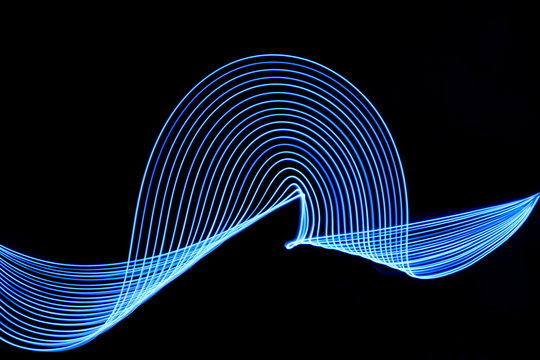 Long exposure photograph of blue neon colour in an abstract swirl, parallel lines pattern against a black background. Light painting photography.