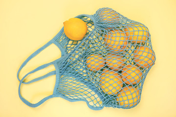 A lot of yellow lemon in the blue mesh bag flat lay on yellow background. Zero waste, eco friendly, no plastic concept. Citrus fruits.