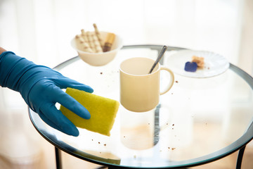Cleaning a dirty table after tea drinking, hand in a blue glove closeup, wipes crumbs.