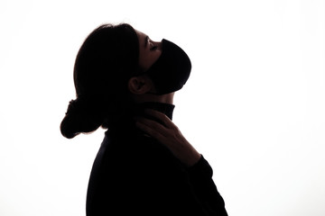 silhouette figure of young woman in protective mask on studio background, girl raised her head up with hands clasped around neck, concept health and safety