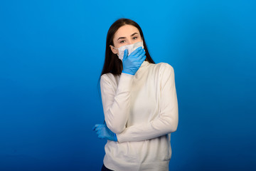 Portrait of a girl in a medical mask, which puts on a rubber glove. Blue background. Copy space.