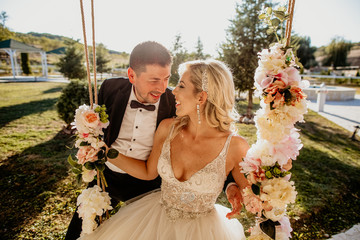 beautiful wedding couple posing on swinger in park. beautiful blonde bride and handsome groom