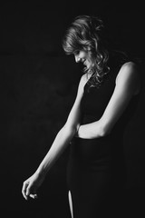 Fototapeta na wymiar Beautiful elegant slim woman in a black dress in a loft studio modestly looks down. Soft selective focus. Black and white art photo.