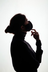 silhouette profile of young woman thinking in protective mask on white studio background, figure of pensive girl, concept health and safety, epidemic problem