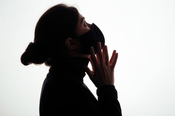 silhouette of young woman in black protective mask covering face on studio background, scared girl looking horrified, concept of panic, information attack, danger