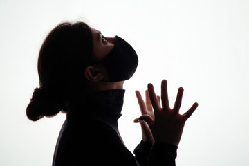 silhouette of young woman in black protective mask covering face on studio background, scared girl looking horrified, concept of panic, information attack, danger